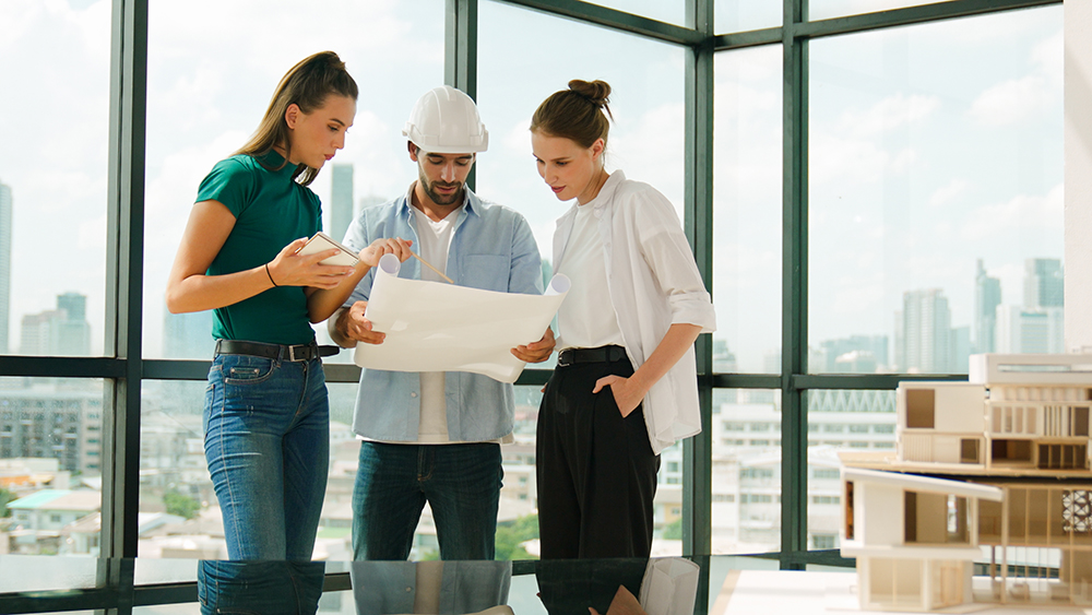Professional architect engineer team talking, sharing, brainstorming about design while manager hold at project plan. Young architect holding plan while manager listen and point at plan. Tracery